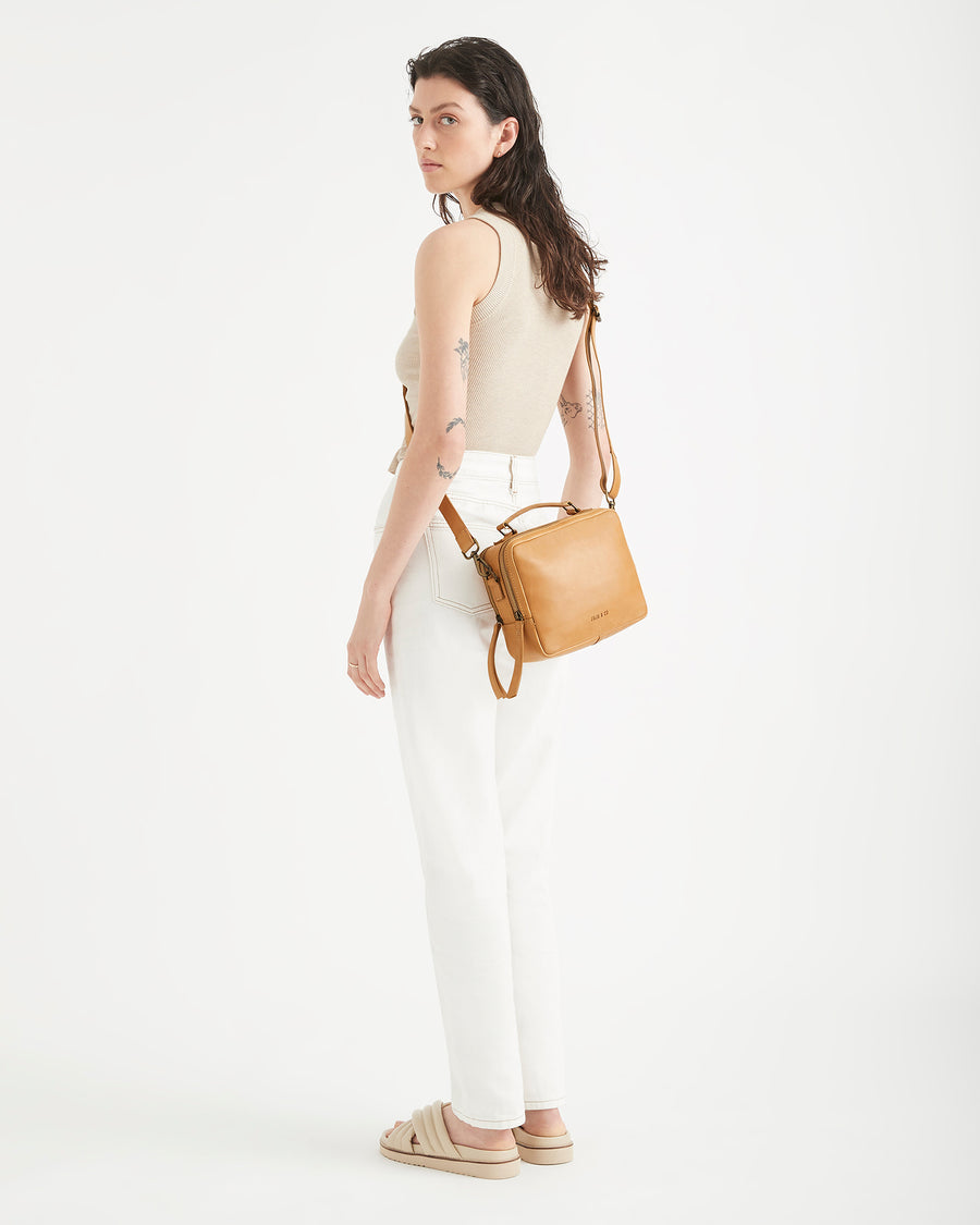 woman standing with tan coloured bag behind her